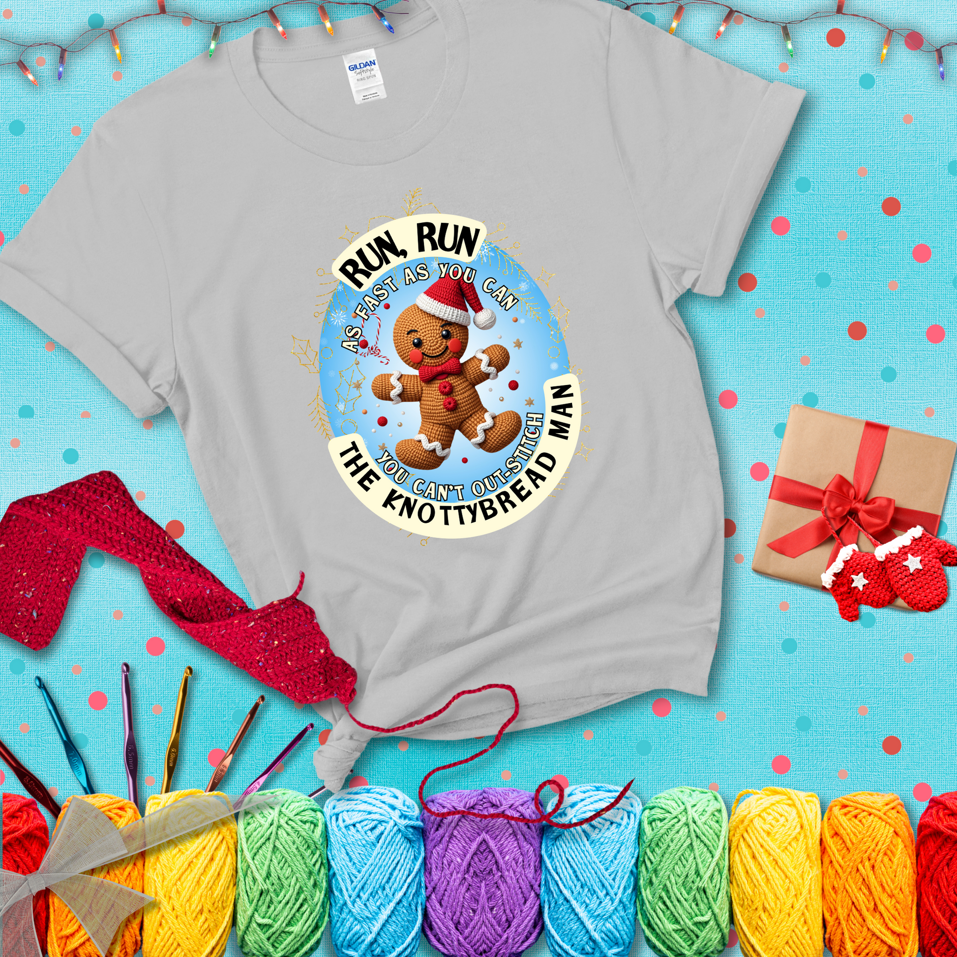Cute crocheted gingerbread man in Santa hat with playful text: “Run, Run As Fast As You Can, You Can’t Out-Stitch the Knottybread Man.” A festive crochet pun shirt, showing a light grey tee with a festive Christmas background