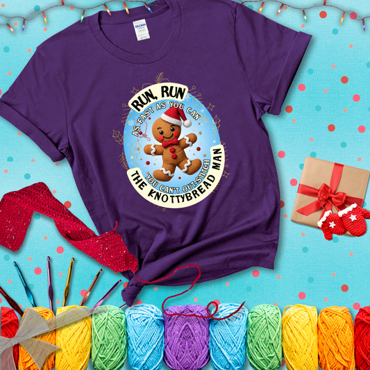 Cute crocheted gingerbread man in Santa hat with playful text: “Run, Run As Fast As You Can, You Can’t Out-Stitch the Knottybread Man.” A festive crochet pun shirt, showing a purple tee with a festive Christmas background