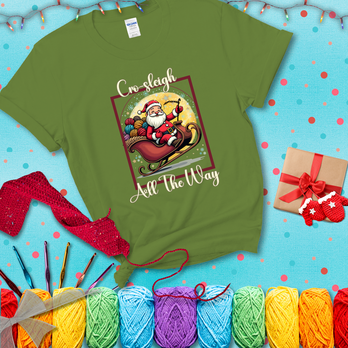 Jolly Santa rides a sleigh overflowing with colorful yarn balls, surrounded by sparkles and holiday cheer. Text reads “Cro-sleigh All the Way" showing a bright green tee with a festive Christmas background