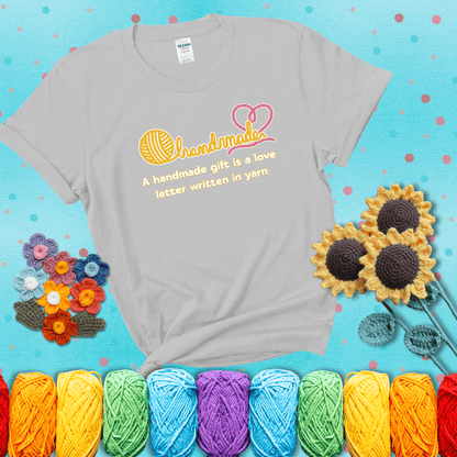 Soft script-style design with heart detail. Text reads: “A Handmade Gift Is a Love Letter Written in Yarn.” A sweet and sentimental shirt for crocheters who craft from the heart, showing a light grey tee with a teal sunflower background