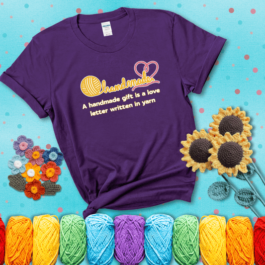 Soft script-style design with heart detail. Text reads: “A Handmade Gift Is a Love Letter Written in Yarn.” A sweet and sentimental shirt for crocheters who craft from the heart, showing a purple tee with a teal sunflower background