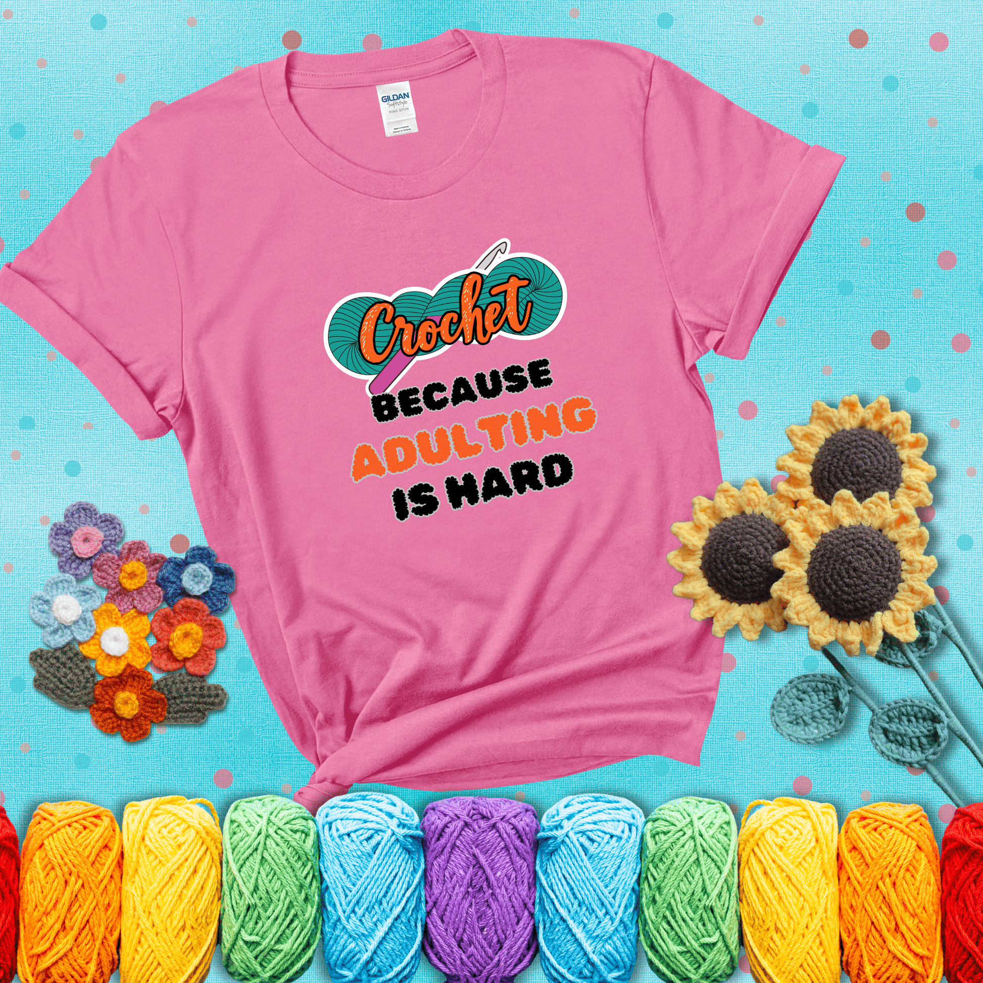 A bold design with the phrase “Crochet Because Adulting Is Hard” featuring a green skein of yarn with a pink crochet hook. The word “Crochet” is in a script font, while “Adulting is hard” is in chunky textured letters showing a pink tee with a teal sunflower background
