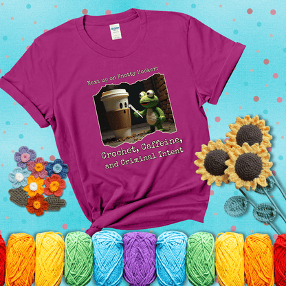 A crocheted frog holding a crochet hook confronts a surprised coffee cup in a dim alleyway with text: "Next up on Knotty Hooker: Crochet, Caffeine, and Criminal Intent," showing a magenta tee with a teal sunflower background