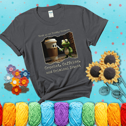 A crocheted frog holding a crochet hook confronts a surprised coffee cup in a dim alleyway with text: "Next up on Knotty Hooker: Crochet, Caffeine, and Criminal Intent," showing a dark grey tee with a teal sunflower background