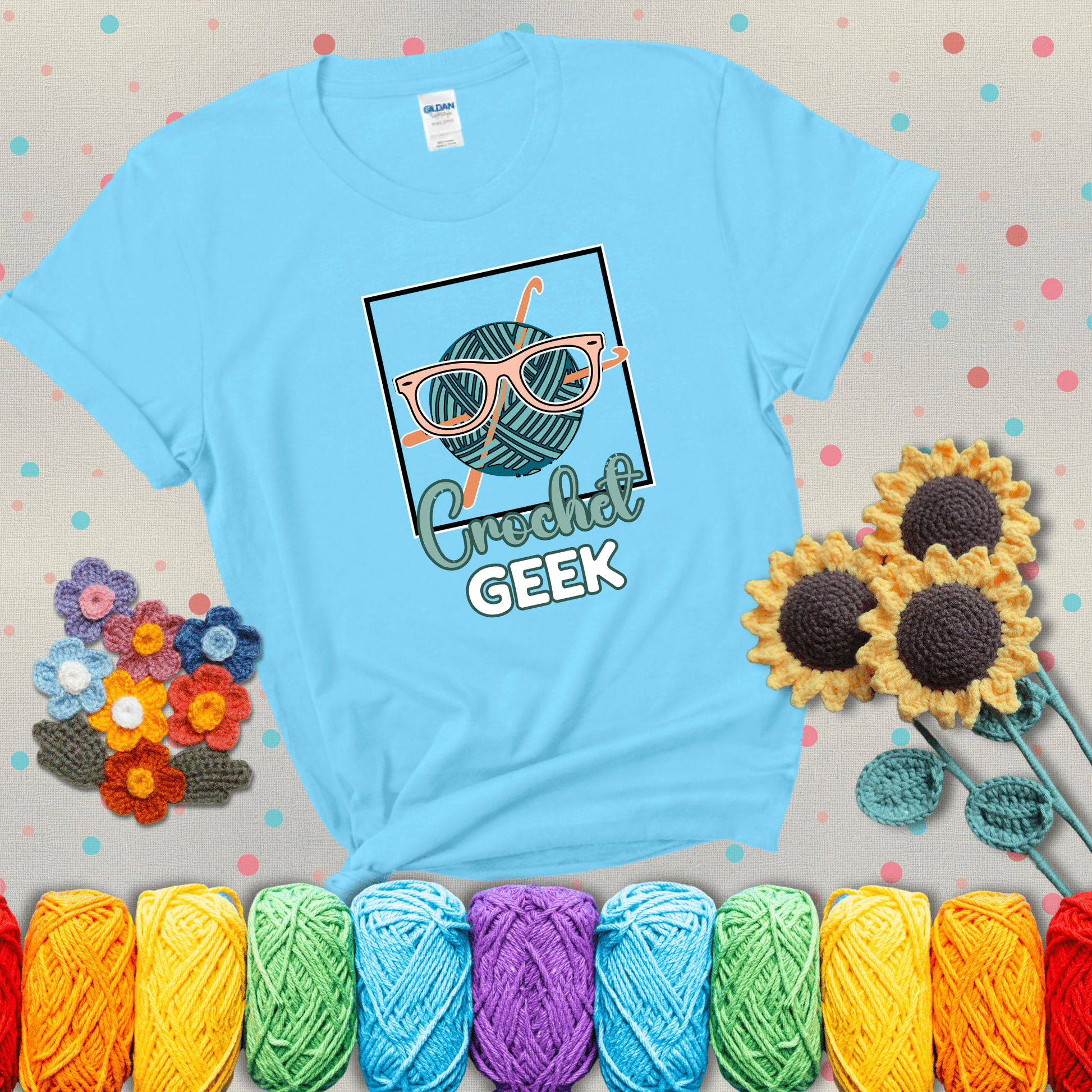 A teal yarn ball with crisscrossed hooks wears oversized nerdy glasses with the phrase “Crochet Geek” in bold, fun text below, showing a light blue tee with grey sunflower background