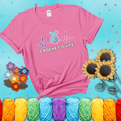 A heartbeat line with a colorful yarn ball and crochet hook in the center, with the words “Crochet is Life”, showing a pink tee with a teal sunflower background
