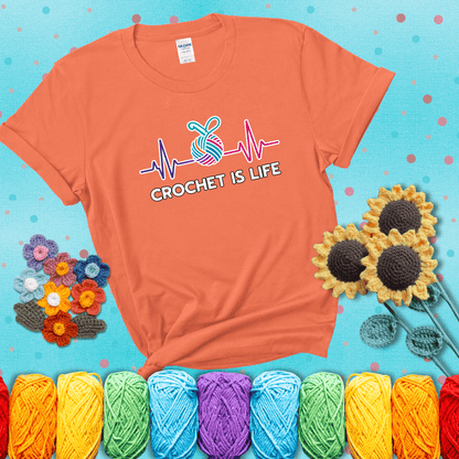 A heartbeat line with a colorful yarn ball and crochet hook in the center, with the words “Crochet is Life”, showing a light orange tee with a teal sunflower background