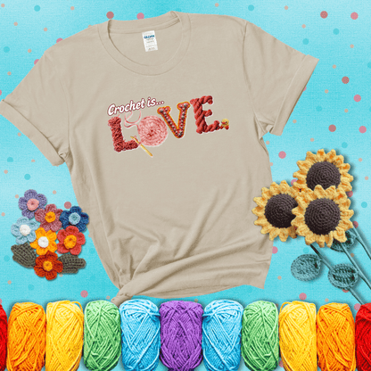 The word "LOVE" spelled with different crochet textures and yarn in red tones, with the phrase “Crochet is…” above in script. showing a dark grey tee with a teal sunflower background