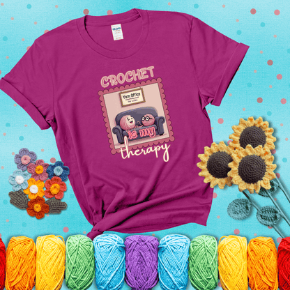 Simple text design with soothing yarn elements. Text reads: “Crochet is My Therapy.” A calming tee for fiber lovers who find healing in every stitch; showing a magenta tee with a teal sunflower background