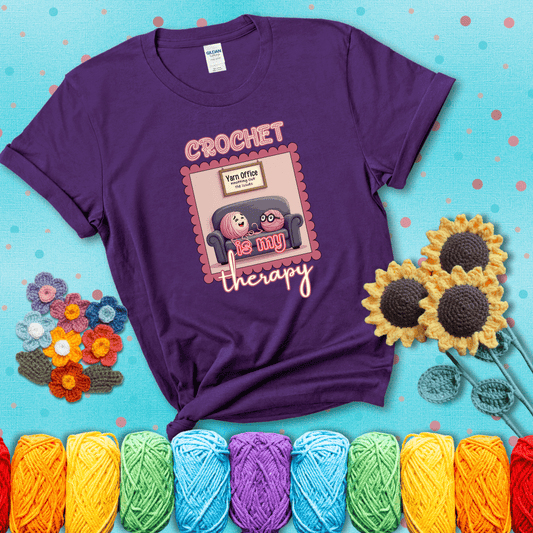 Simple text design with soothing yarn elements. Text reads: “Crochet is My Therapy.” A calming tee for fiber lovers who find healing in every stitch; showing a purple tee with a teal sunflower background