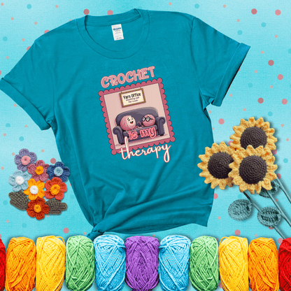 Simple text design with soothing yarn elements. Text reads: “Crochet is My Therapy.” A calming tee for fiber lovers who find healing in every stitch; showing a blue-green tee with a teal sunflower background