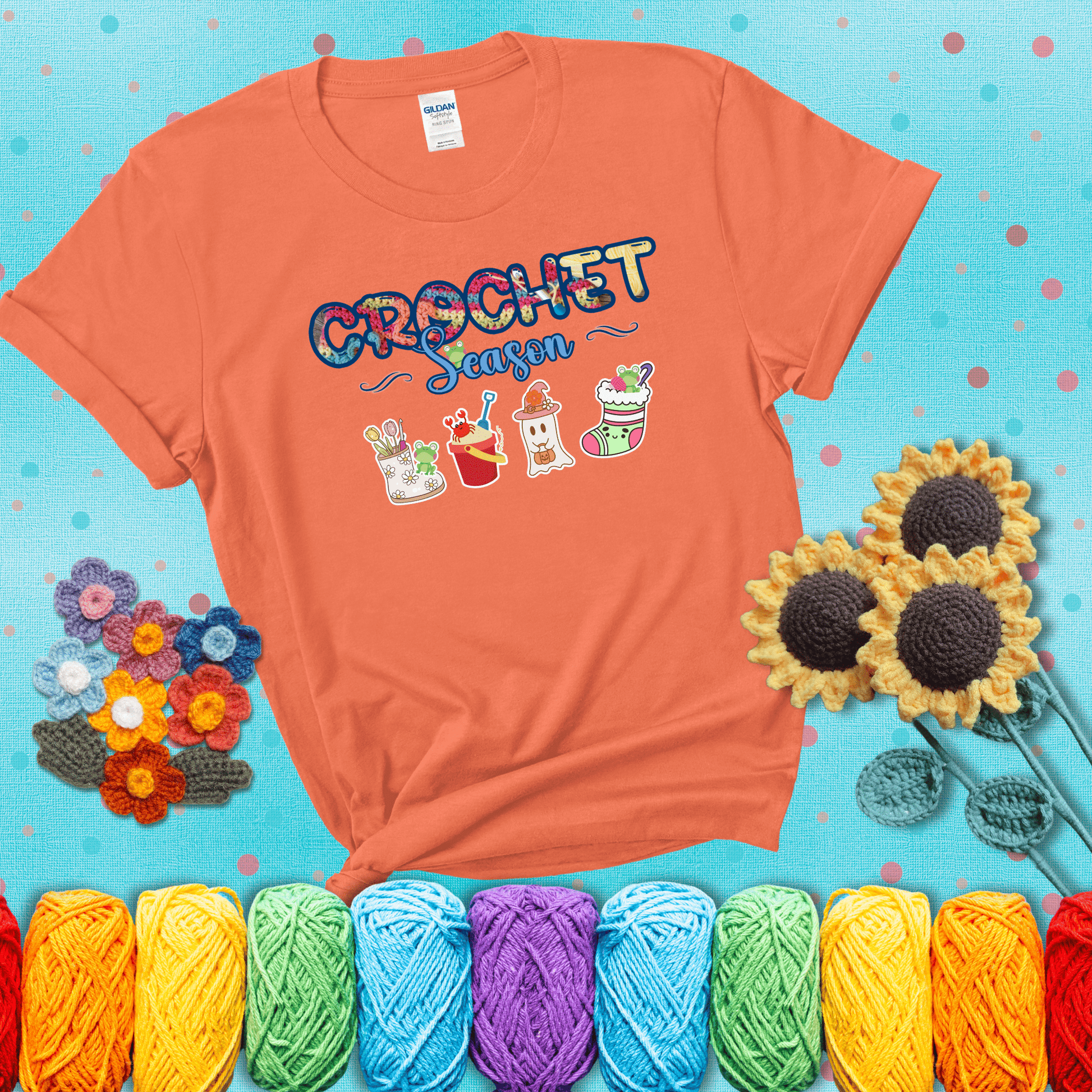 The words “Crochet Season” with cute seasonal icons below: a spring boot with hooks, summer bucket with crab, fall ghost with pumpkin hat, and winter stocking - all with tiny frogs; showing a light orange tee with a teal sunflower background