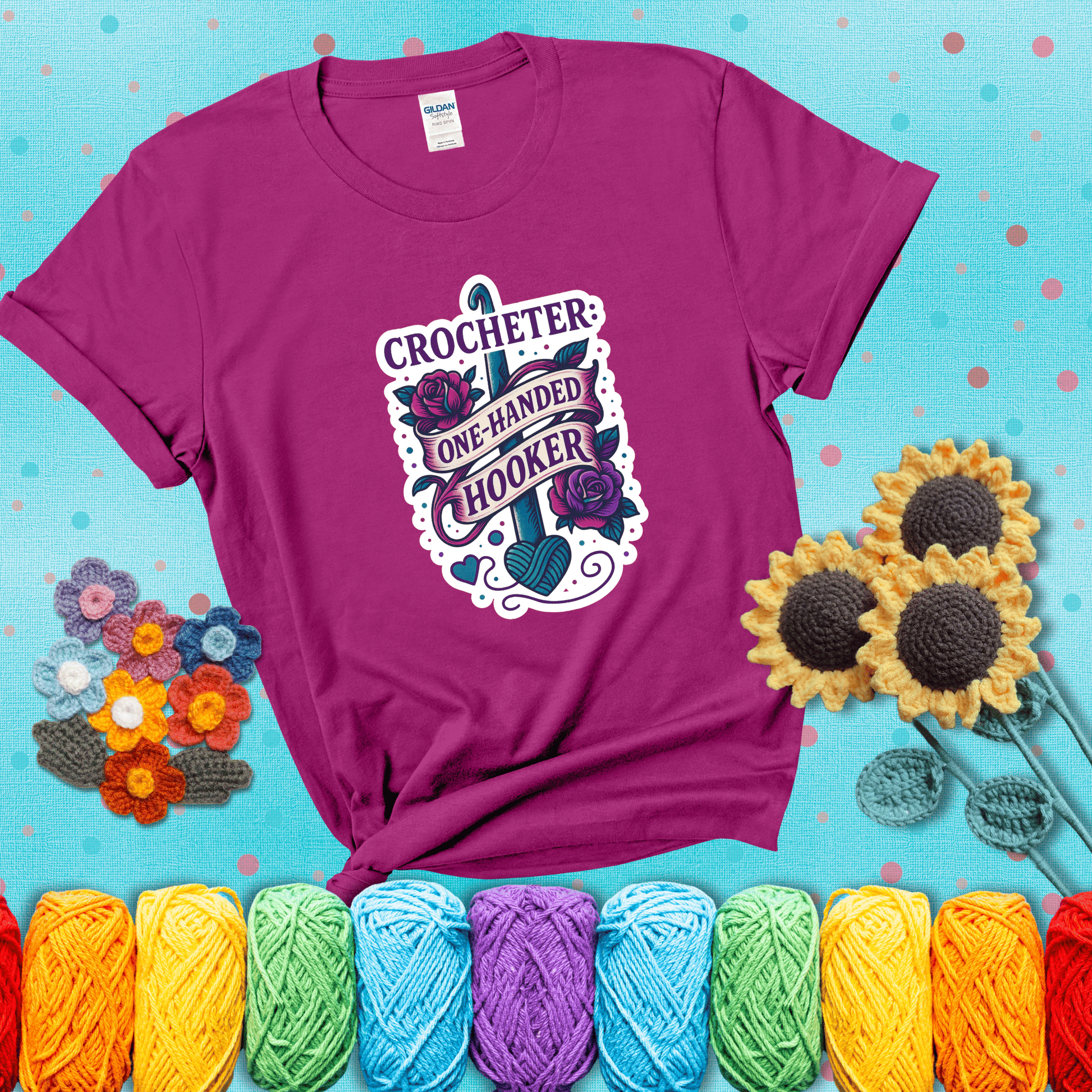 Tattoo-style design with a crochet hook, roses, and banner that says "Crocheter: One-Handed Hooker" showing a magenta tee with a teal sunflower background