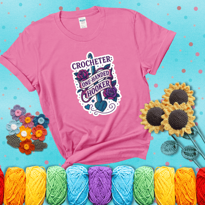 Tattoo-style design with a crochet hook, roses, and banner that says "Crocheter: One-Handed Hooker" showing a pink tee with a teal sunflower background