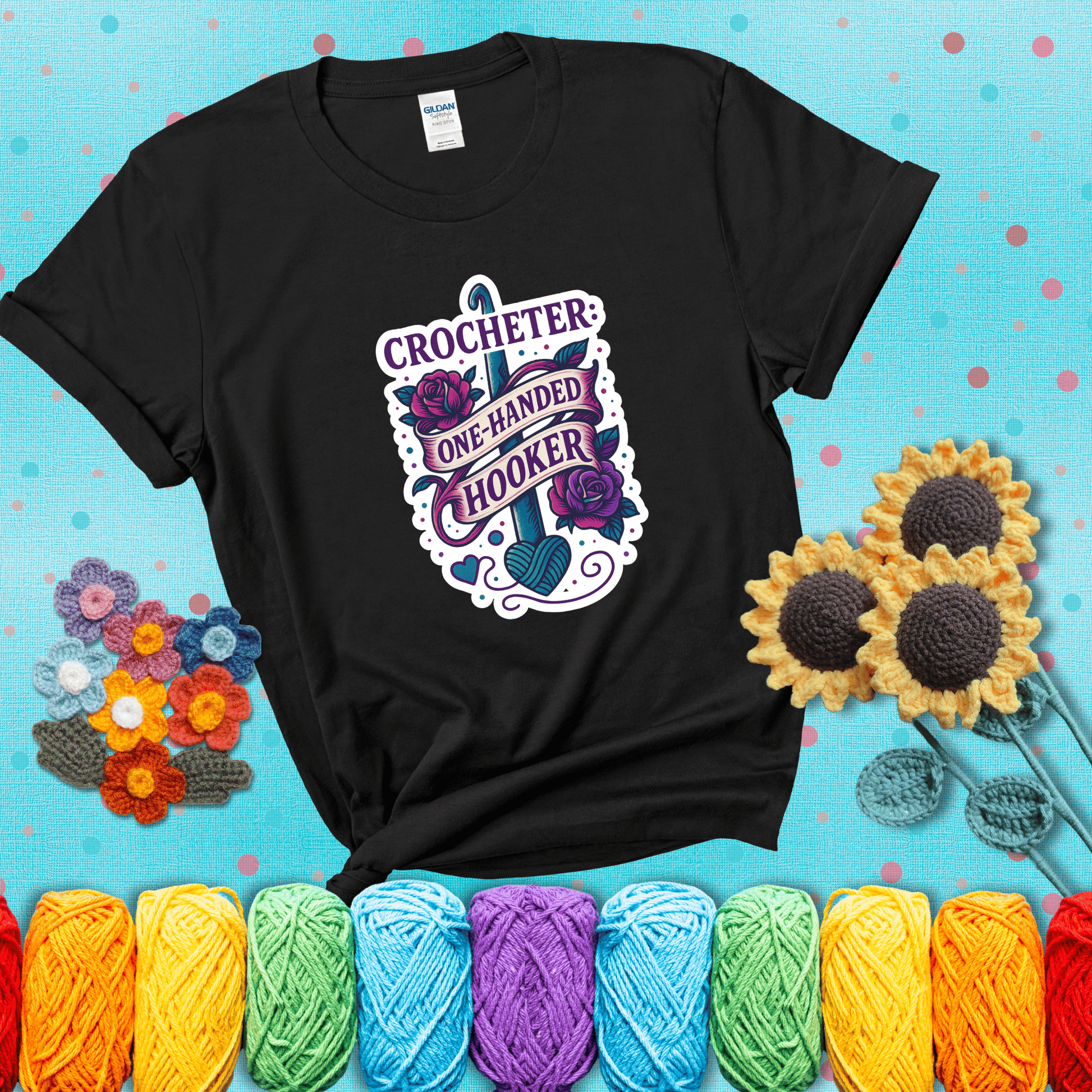 Tattoo-style design with a crochet hook, roses, and banner that says "Crocheter: One-Handed Hooker" showing a black tee with a teal sunflower background