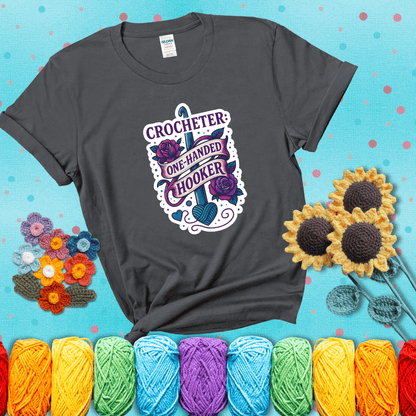 Tattoo-style design with a crochet hook, roses, and banner that says "Crocheter: One-Handed Hooker" showing a dark grey tee with a teal sunflower background