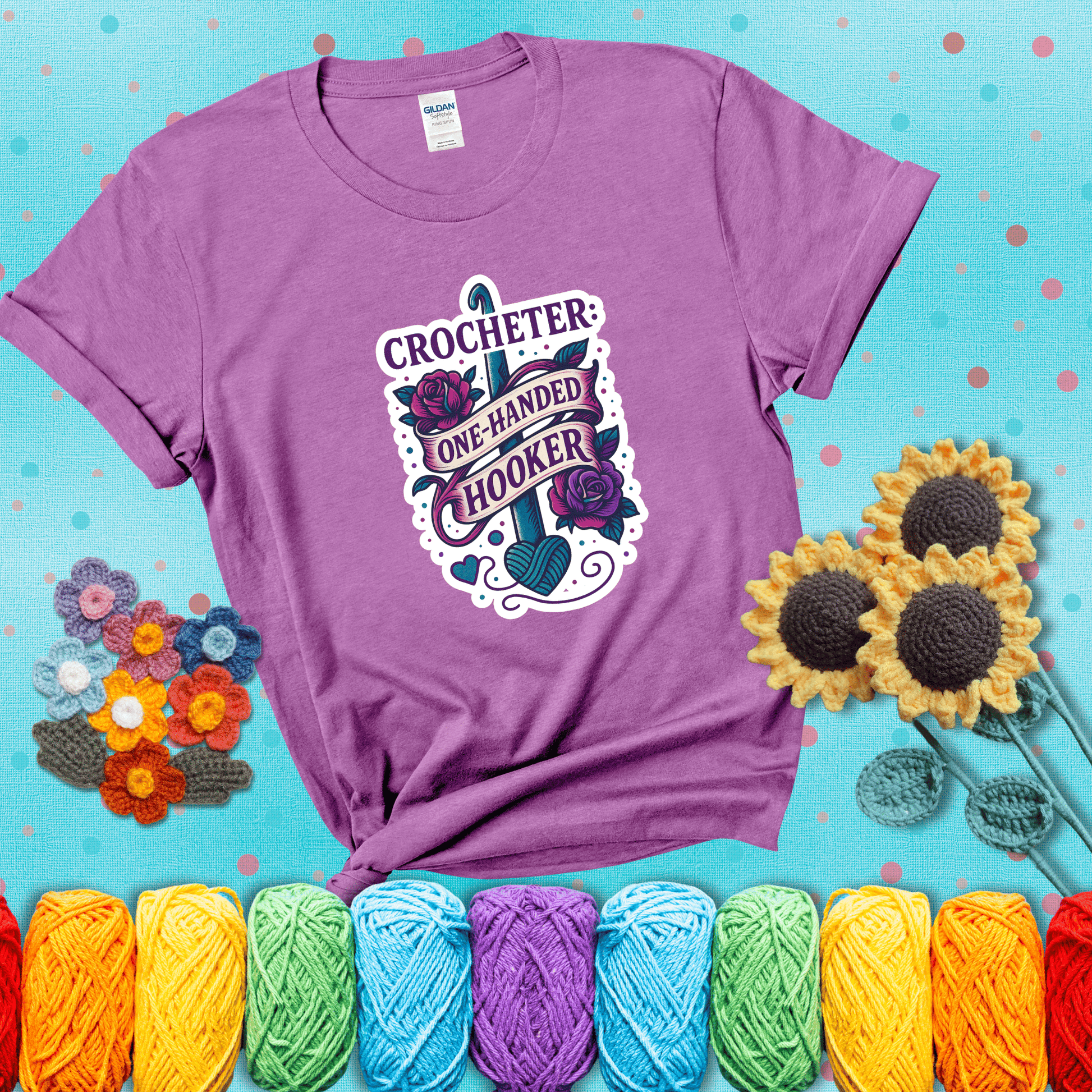 Tattoo-style design with a crochet hook, roses, and banner that says "Crocheter: One-Handed Hooker" showing a light purple tee with a teal sunflower background