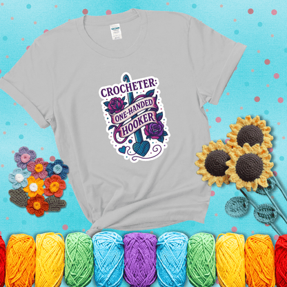 Tattoo-style design with a crochet hook, roses, and banner that says "Crocheter: One-Handed Hooker" showing a light grey tee with a teal sunflower background