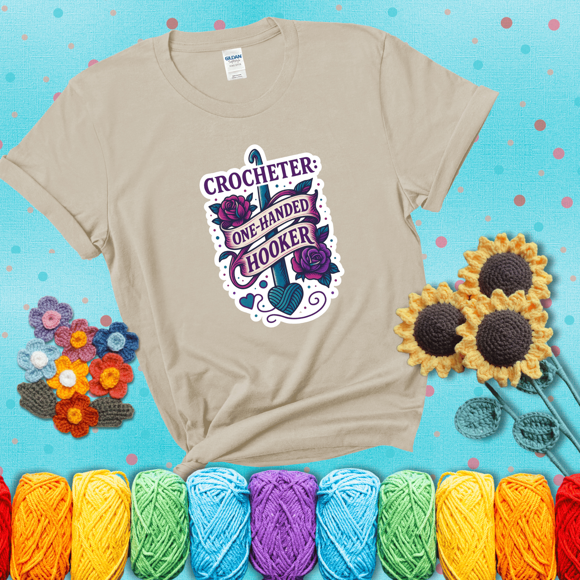 Tattoo-style design with a crochet hook, roses, and banner that says "Crocheter: One-Handed Hooker" showing a beige tee with a teal sunflower background