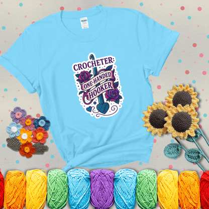 Tattoo-style design with a crochet hook, roses, and banner that says "Crocheter: One-Handed Hooker" showing a light blue tee with grey sunflower background