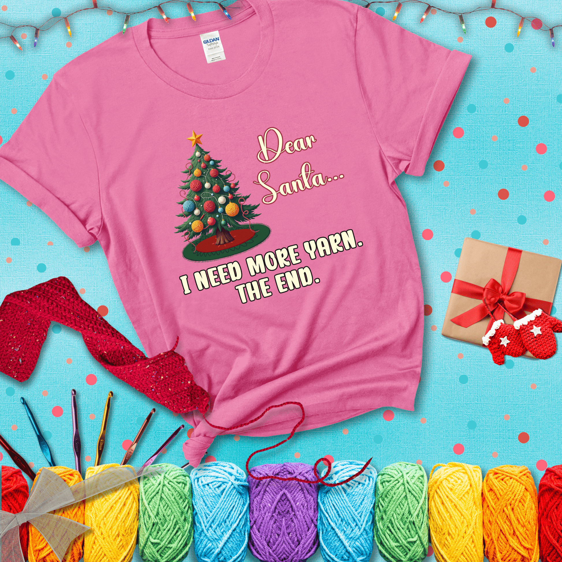 Christmas tree decorated with yarn ball ornaments and a stitched message that reads “Dear Santa… I Need More Yarn. The End.” Whimsical holiday yarn-lover shirt, showing a pink tee with a festive Christmas background