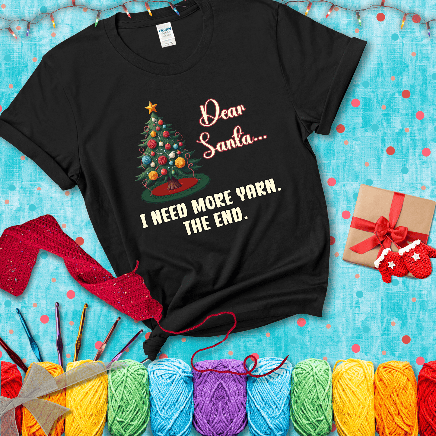 Christmas tree decorated with yarn ball ornaments and a stitched message that reads “Dear Santa… I Need More Yarn. The End.” Whimsical holiday yarn-lover shirt, showing a black tee with a festive Christmas background