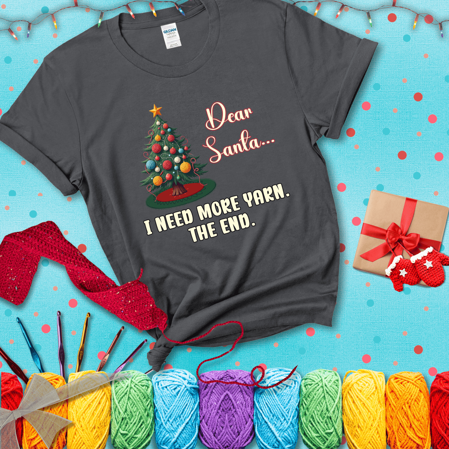 Christmas tree decorated with yarn ball ornaments and a stitched message that reads “Dear Santa… I Need More Yarn. The End.” Whimsical holiday yarn-lover shirt, showing a dark grey tee with a festive Christmas background