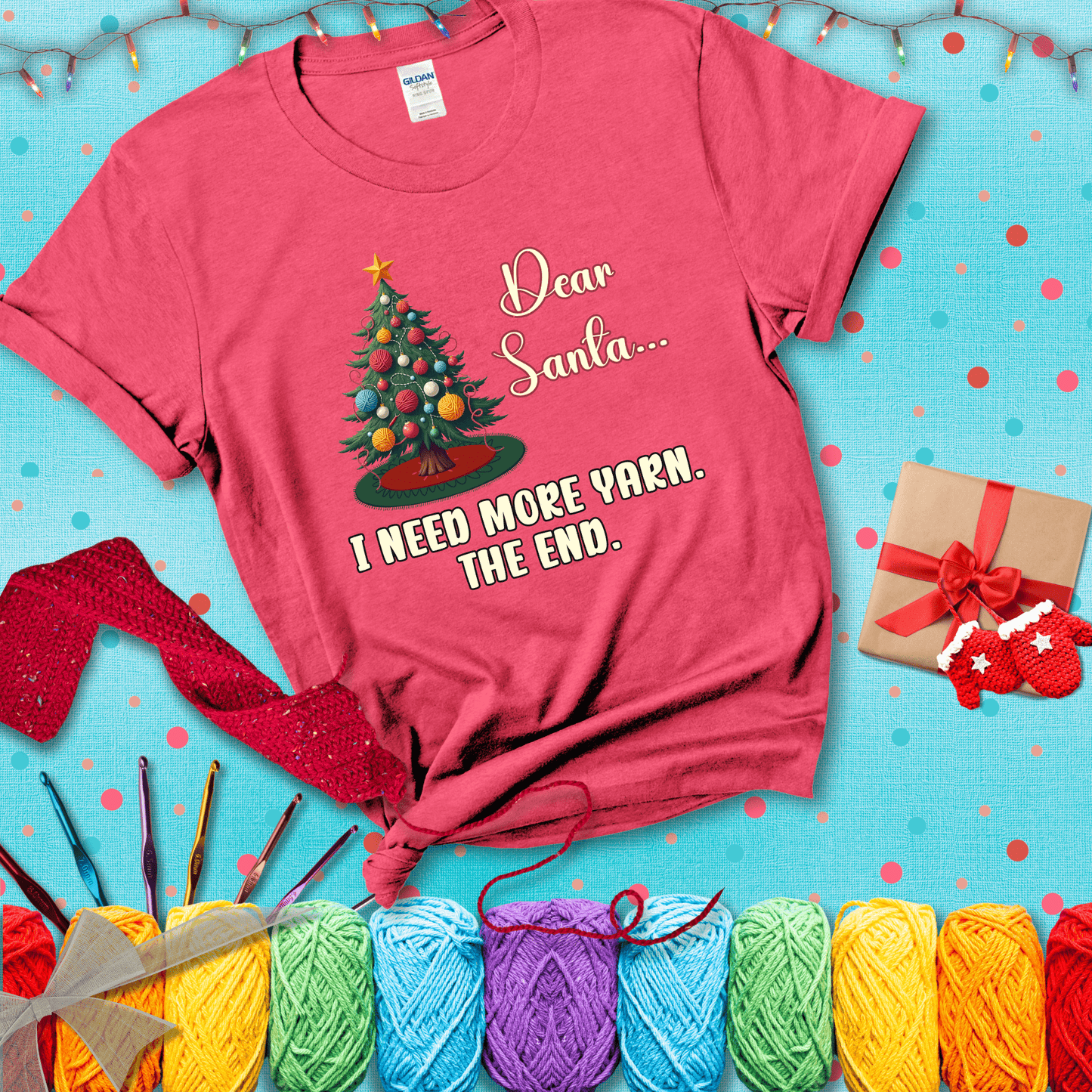 Christmas tree decorated with yarn ball ornaments and a stitched message that reads “Dear Santa… I Need More Yarn. The End.” Whimsical holiday yarn-lover shirt, showing a light red tee with a festive Christmas background