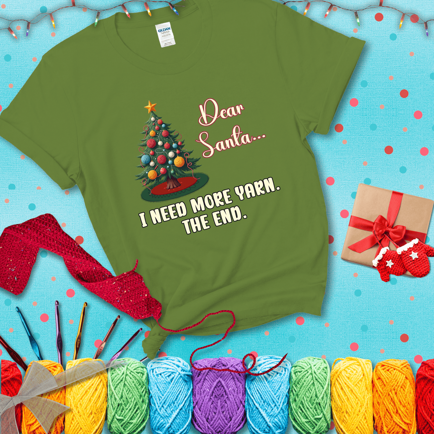 Christmas tree decorated with yarn ball ornaments and a stitched message that reads “Dear Santa… I Need More Yarn. The End.” Whimsical holiday yarn-lover shirt, showing a bright green tee with a festive Christmas background