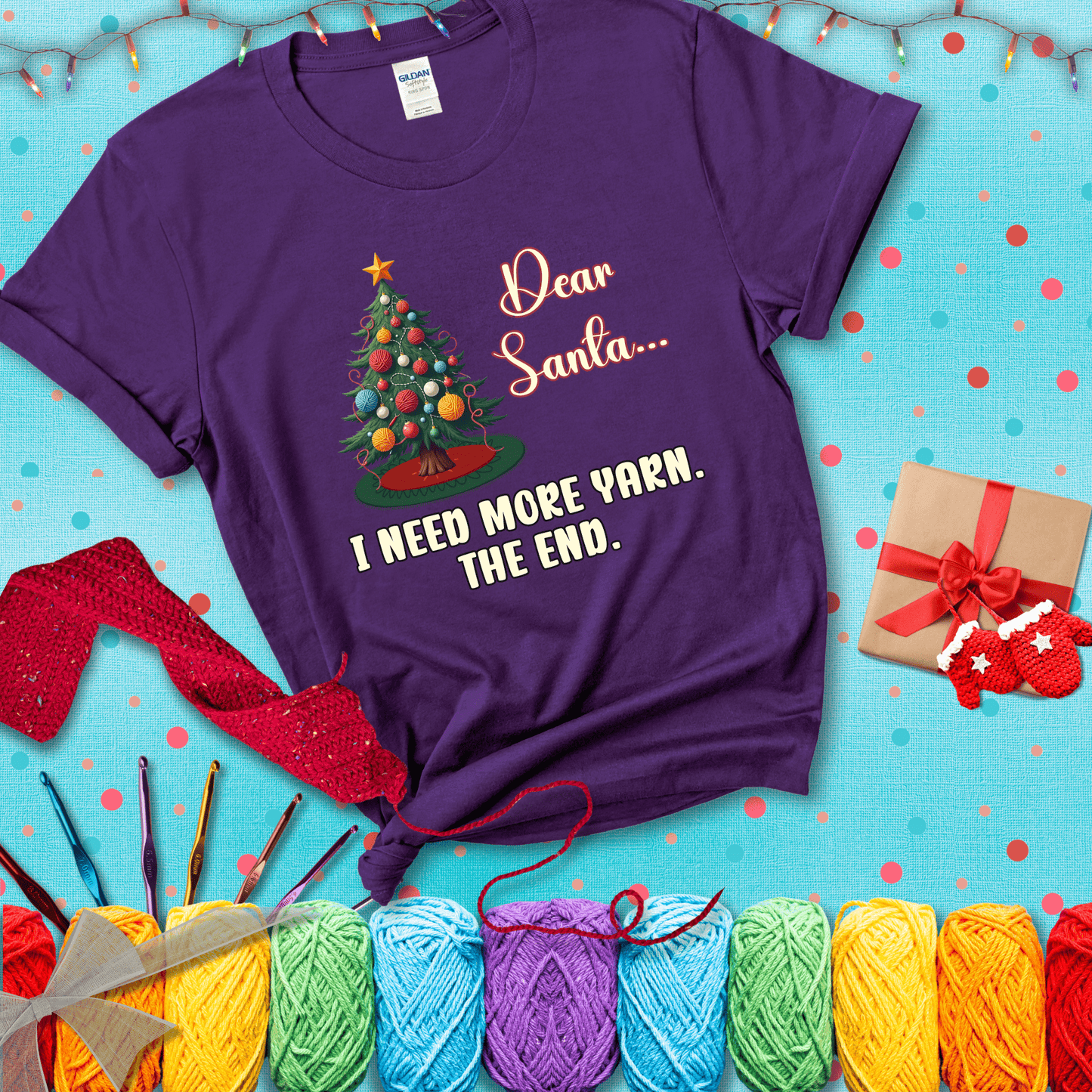 Christmas tree decorated with yarn ball ornaments and a stitched message that reads “Dear Santa… I Need More Yarn. The End.” Whimsical holiday yarn-lover shirt, showing a purple tee with a festive Christmas background