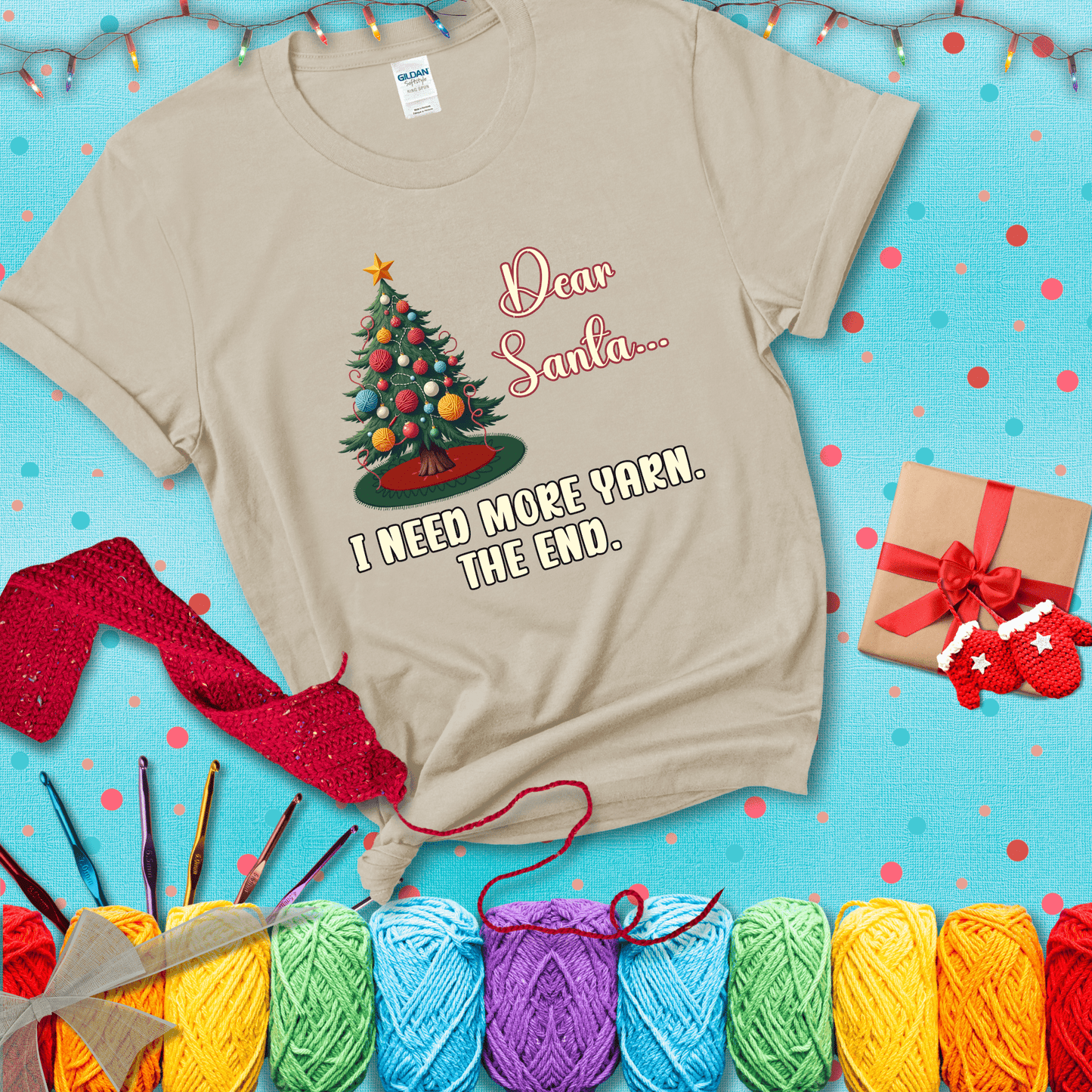 Christmas tree decorated with yarn ball ornaments and a stitched message that reads “Dear Santa… I Need More Yarn. The End.” Whimsical holiday yarn-lover shirt, showing a beige tee with a festive Christmas background