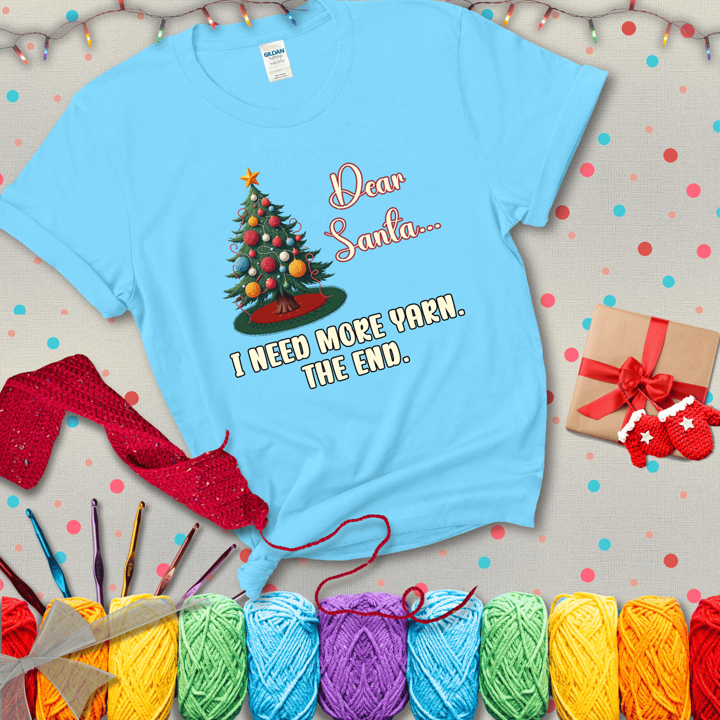 Christmas tree decorated with yarn ball ornaments and a stitched message that reads “Dear Santa… I Need More Yarn. The End.” Whimsical holiday yarn-lover shirt, showing a light blue tee with a festive Christmas background