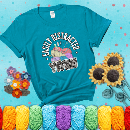 If yarn steals your focus every Design reads 'Easily Distracted By Yarn', perfect crochet gift for yarn lovers; showing a blue-green tee with a teal sunflower background