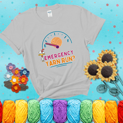 A fuel gauge with a ball of yarn as the needle pointing to empty, a frantic chicken, and the text “Emergency Yarn Run?” showing a light grey tee with a teal sunflower background
