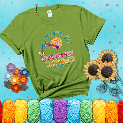 A fuel gauge with a ball of yarn as the needle pointing to empty, a frantic chicken, and the text “Emergency Yarn Run?” showing a bright green tee with a teal sunflower background