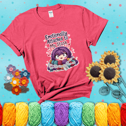 Rows of colorful yarn skeins stacked with playful text. Text reads: “Emotionally Attached to My Stash.” A humorous shirt for fiber lovers with growing collections, showing a light red tee with a teal sunflower background