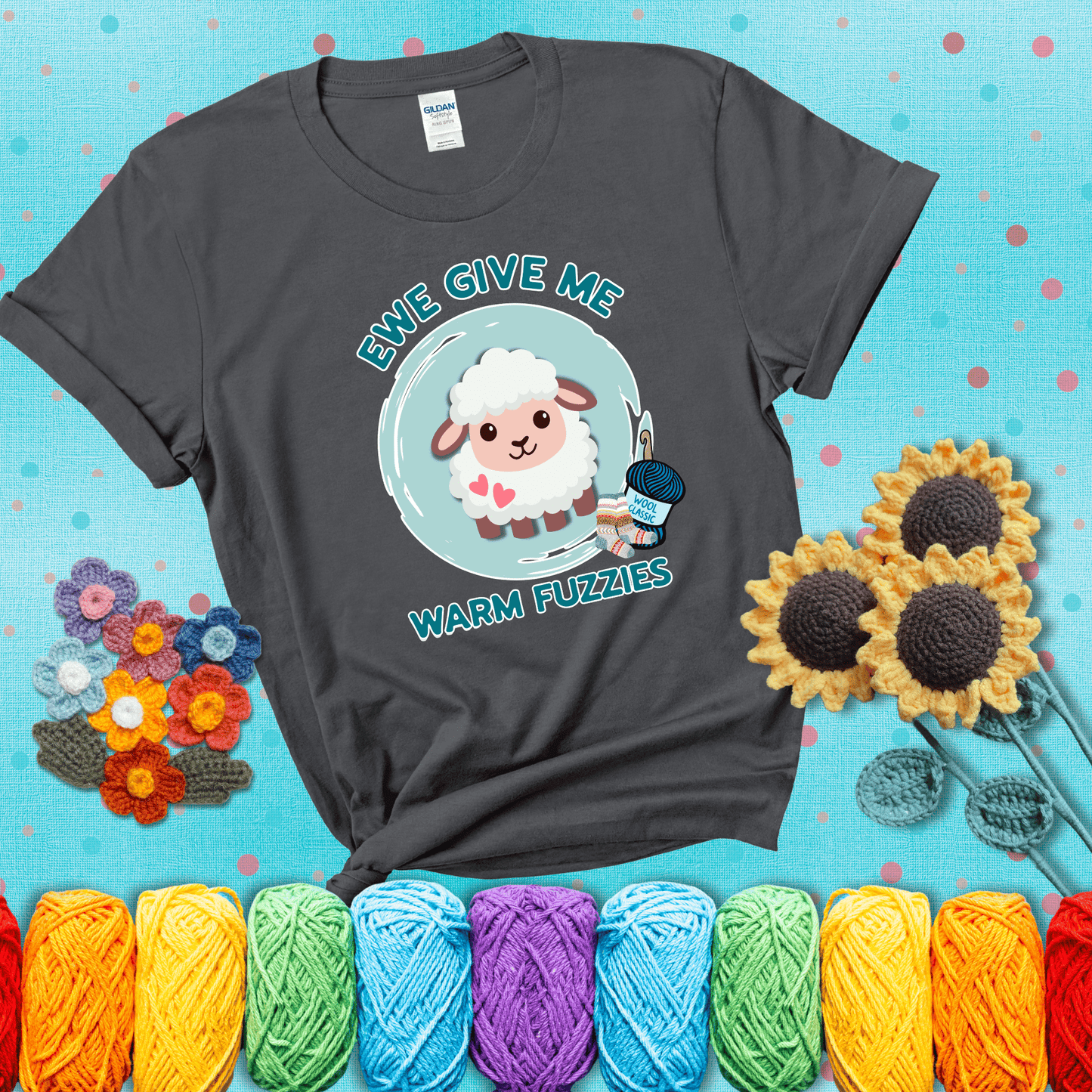 Cartoon sheep with pink hearts, wool socks, and yarn labeled “Wool Classic.” Text reads “Ewe Give Me Warm Fuzzies” showing a dark grey tee with a teal sunflower background