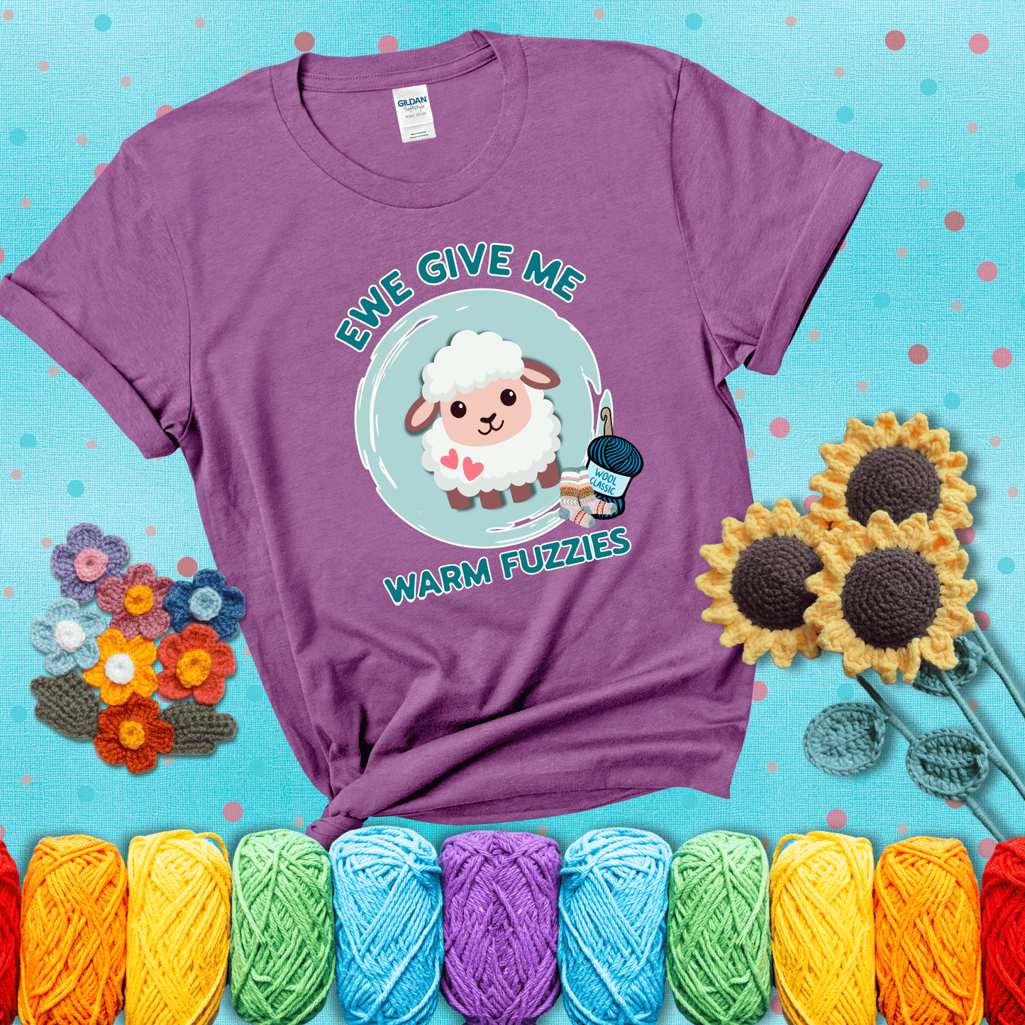 Cartoon sheep with pink hearts, wool socks, and yarn labeled “Wool Classic.” Text reads “Ewe Give Me Warm Fuzzies” showing a light purple tee with a teal sunflower background