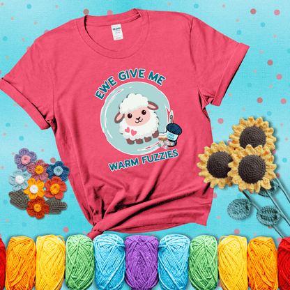 Cartoon sheep with pink hearts, wool socks, and yarn labeled “Wool Classic.” Text reads “Ewe Give Me Warm Fuzzies” showing a light red tee with a teal sunflower background