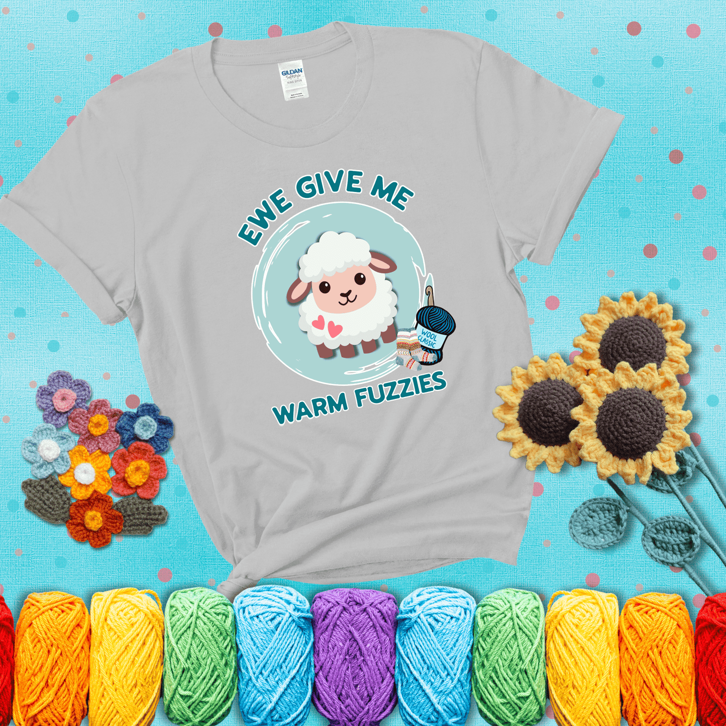 Cartoon sheep with pink hearts, wool socks, and yarn labeled “Wool Classic.” Text reads “Ewe Give Me Warm Fuzzies” showing a light grey tee with a teal sunflower background