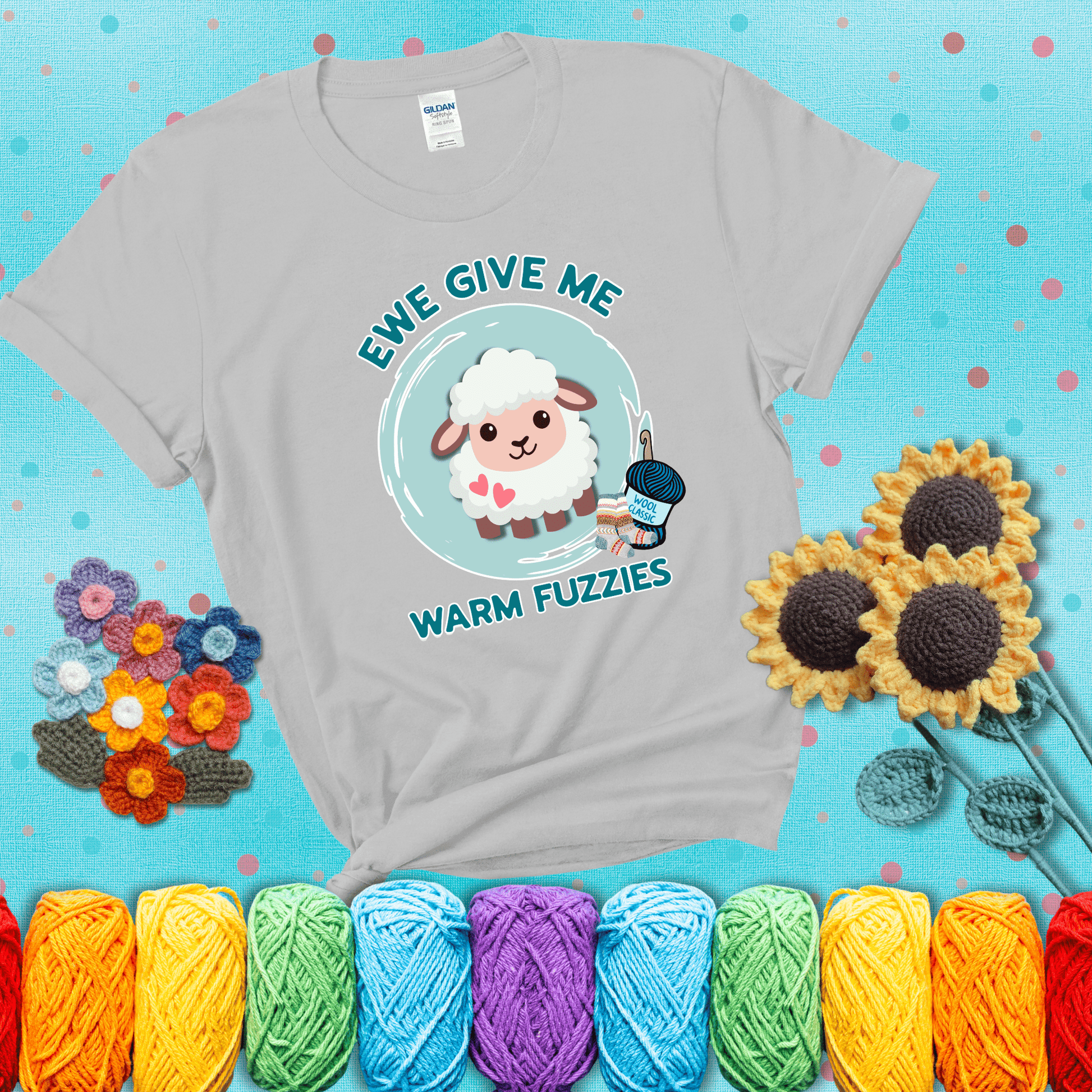 Cartoon sheep with pink hearts, wool socks, and yarn labeled “Wool Classic.” Text reads “Ewe Give Me Warm Fuzzies” showing a light grey tee with a teal sunflower background