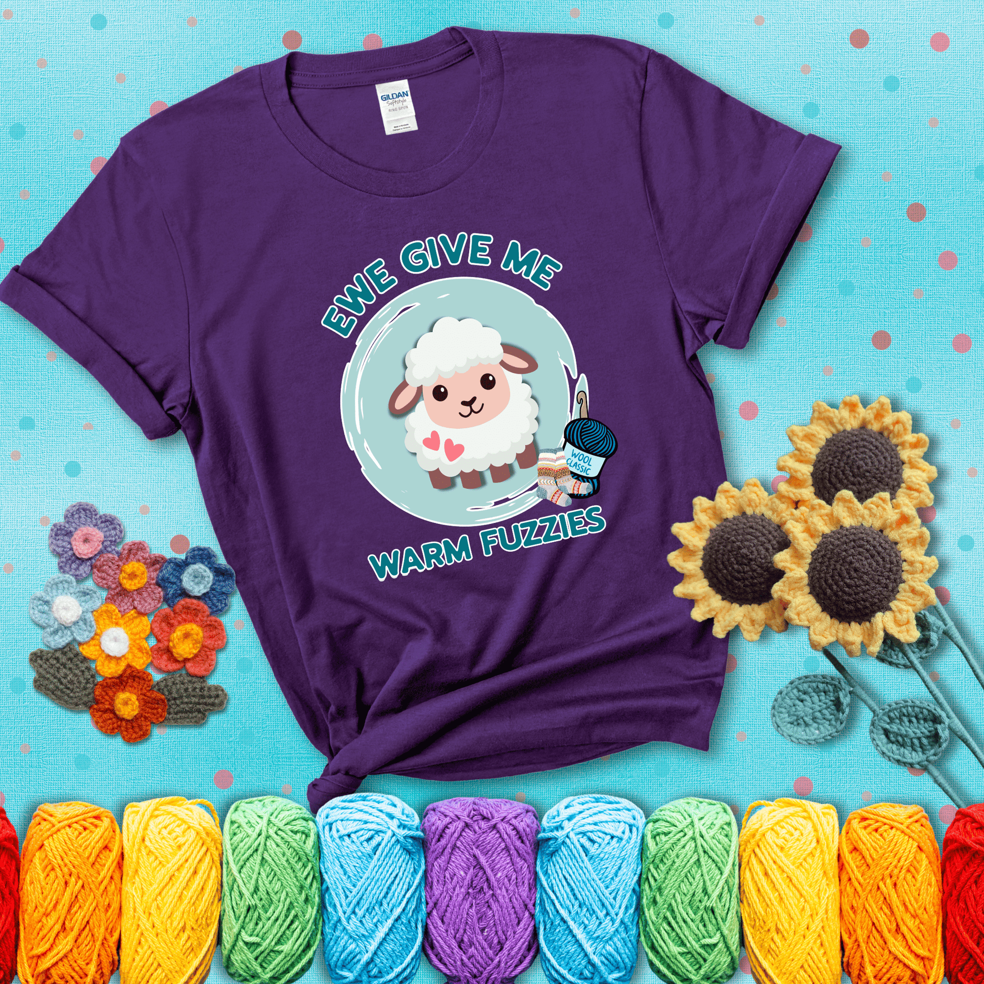 Cartoon sheep with pink hearts, wool socks, and yarn labeled “Wool Classic.” Text reads “Ewe Give Me Warm Fuzzies” showing a purple tee with a teal sunflower background