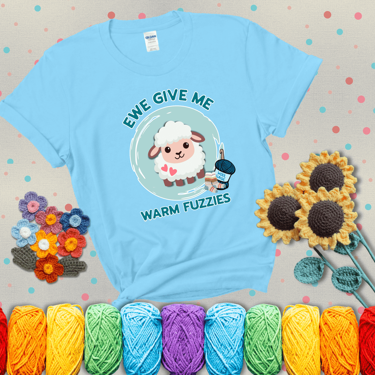 Cartoon sheep with pink hearts, wool socks, and yarn labeled “Wool Classic.” Text reads “Ewe Give Me Warm Fuzzies” showing a light blue tee with grey sunflower background