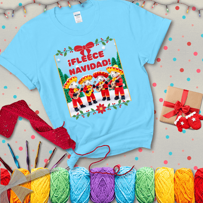 Four crocheted sheep dressed in red mariachi outfits with guitars, standing in a snowy scene under the phrase “¡Fleece Navidad!” showing a light blue tee with a festive Christmas background
