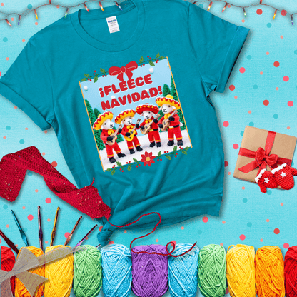 Four crocheted sheep dressed in red mariachi outfits with guitars, standing in a snowy scene under the phrase “¡Fleece Navidad!” showing a blue-green tee with a festive Christmas background