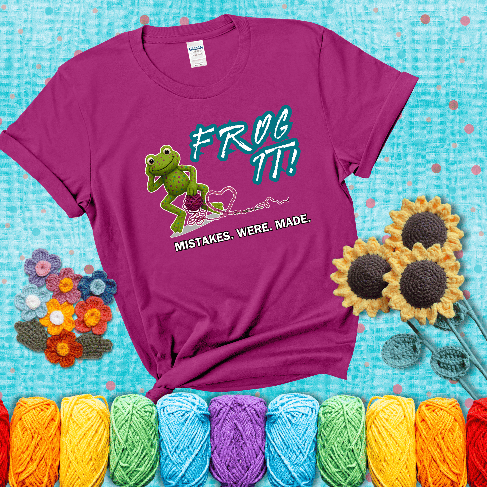 Green frog with yarn and heart-shaped loop. Text reads: “Frog It! Mistakes Were Made.” A playful crochet tee for anyone who's ever had to rip it back, showing a magenta tee with a teal sunflower background