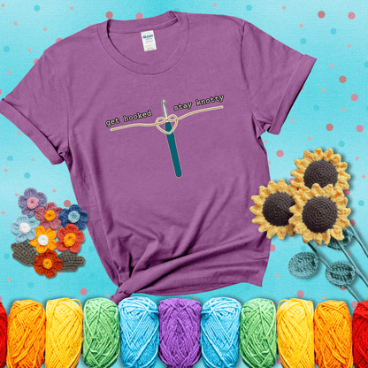 Hooked on yarn? Same Design reads 'Get Hooked, Stay Knotty' , perfect crochet gift for yarn lovers, showing a light purple tee with a teal sunflower background