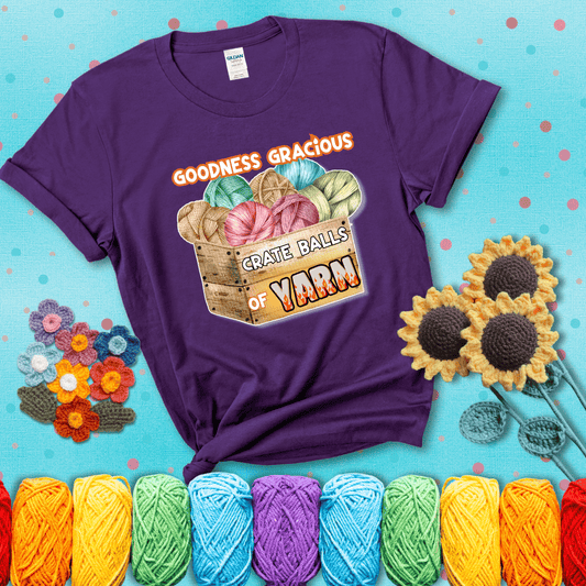 Wooden crate filled with colorful yarn balls and bold text “Goodness Gracious, Crate Balls of Yarn” with flame effects, a funny gift for crocheters showing a purple tee with a teal sunflower background