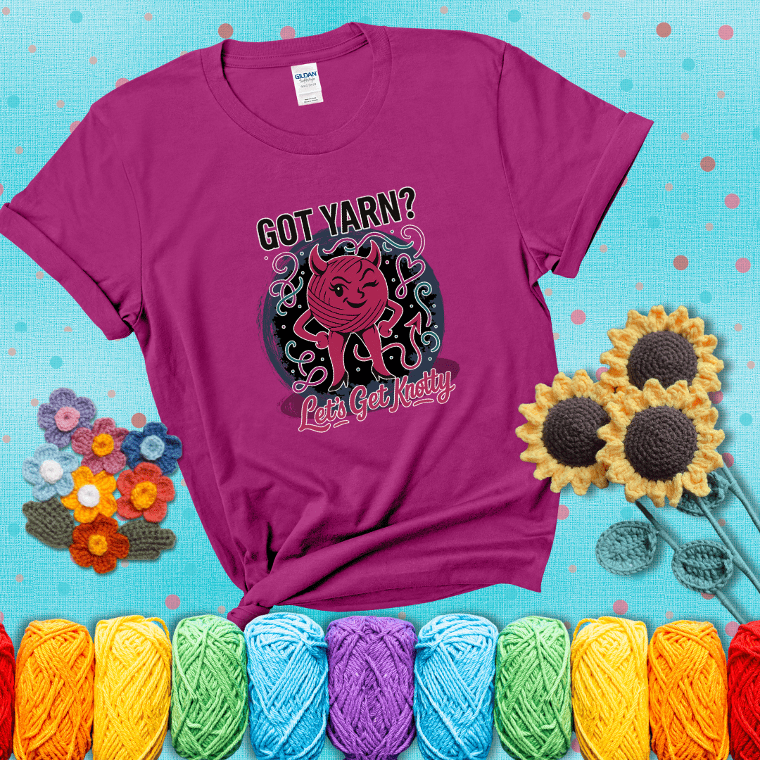 A cheeky pink yarn ball with devil horns, arms, and legs winks under the text “Got Yarn? Let’s Get Knotty,” showing a magenta tee with a teal sunflower background