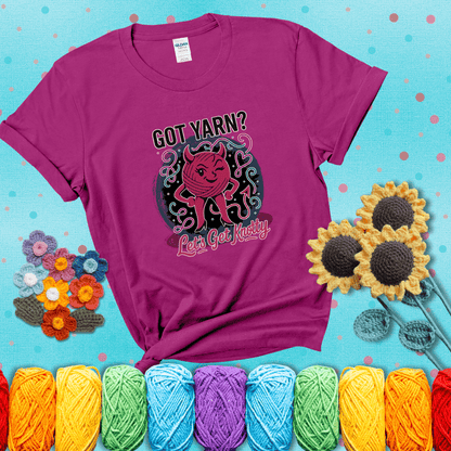 A cheeky pink yarn ball with devil horns, arms, and legs winks under the text “Got Yarn? Let’s Get Knotty,” showing a magenta tee with a teal sunflower background